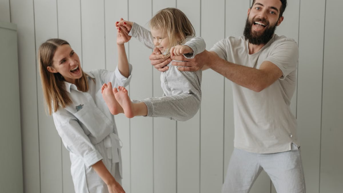 Joyful parents playing with their daughter indoors, all wearing white, capturing a moment of happiness.